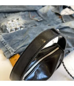 Dettaglio della borsa a bauletto nera lucida con manici curvi e zip argentata di precisione