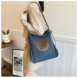 Close-up of denim canvas tote with brown leather shoulder strap and ZC JP logo detail