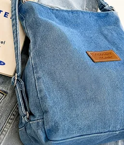 Dettaglio della borsa tote in denim blu lavato con etichetta in pelle marrone e cuciture