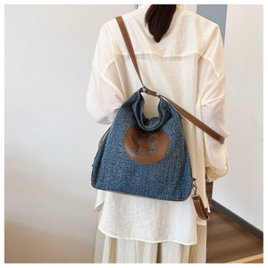 Rear view of model wearing a navy denim hobo bag with brown leather strap and logo patch