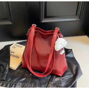 Detail of burgundy glossy tote bag with plush white cloud pendant on black jacket