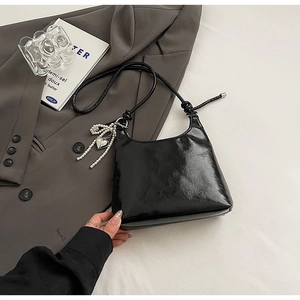Detail of black glossy shoulder bag with heart pearl pendant and knotted strap