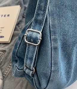 Dettaglio della borsa in denim blu con fibbia in metallo argento e cuciture a contrasto fitte