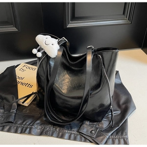 Detail of black tote bag with plush charm on leather jacket background