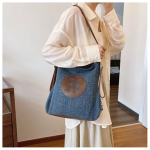 Detail of blue denim shoulder bag with brown leather logo patch and silver metal clasp