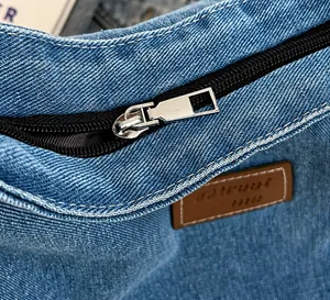 Dettaglio della cerniera in metallo argentato e patch in pelle su borsa in denim blu