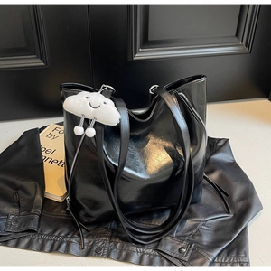Macro shot of glossy black tote bag with plush cloud charm on a leather jacket background