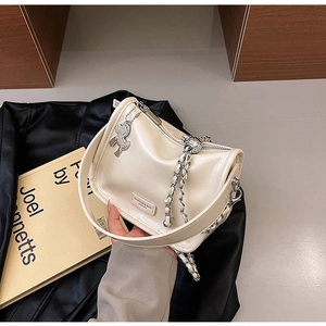 Détail d'un sac demi-lune crème avec chaîne argentée et plaque de marque en métal