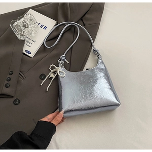 Detail of silver metallic pleated bucket bag with pearl bow charm on grey blazer