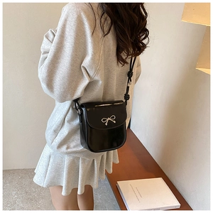 Detail of black faux leather crossbody bag with a silver metal bow clasp on the flap