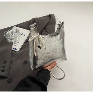 Detail of silver pleated handbag with pearl bow and heart charm on blazer background