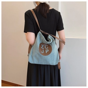 Detail of light blue denim tote with brown leather straps shown on a model's back