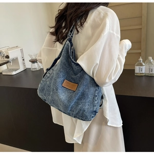 Dettaglio di una capiente borsa in denim lavato blu con logo in pelle marrone stile vintage