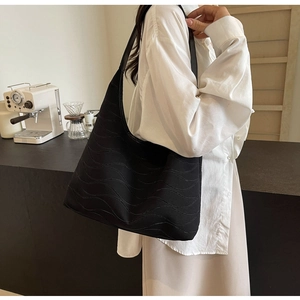 Detail of a black quilted tote bag with wave stitching on a model's shoulder in soft light