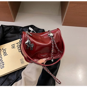 Détail d'un sac bandoulière bordeaux en cuir avec chaîne argentée et pendentif cheval