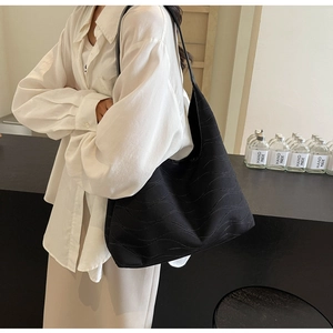 Close-up of the wave-textured surface and slim shoulder strap on the large black tote bag