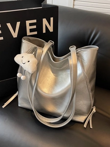 Silver metallic tote bag with plush cloud pendant on a leather sofa for casual use