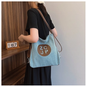 Close-up of light blue denim tote bag with brown leather straps and ZCJP logo patch
