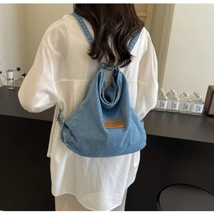 Dettaglio di uno zaino in denim azzurro con toppa in pelle sulla schiena del modello