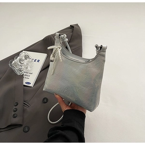 Close-up of holographic silver shoulder bag with textured pleats and a pearl bow charm