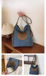 Detail of dark blue denim tote bag featuring brown leather patch and shoulder straps