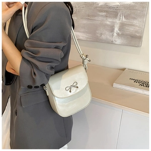 Detail of cream saddle bag with metal bow accent and knotted cord strap styling