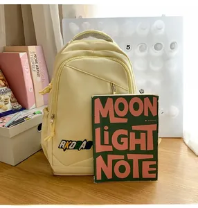 Detail view of a pale yellow backpack with AKOBA embroidery and multi-zipper compartments