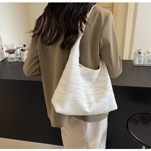 Detail of white tote bag with wavy 3D texture shown on model in a cafe setting