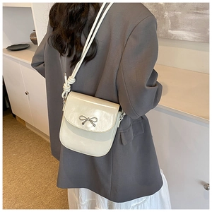 Detailed view of cream white crossbody bag with silver bow accent on gray suit