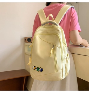 Detail of light yellow nylon backpack showing AKDBAG embroidery and multi-pocket layout