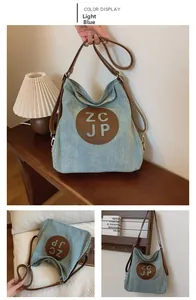 Detail of light blue denim shoulder bag featuring a round brown leather logo and strap