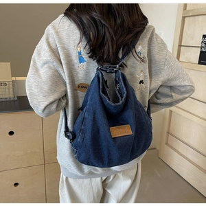 Dettaglio dello zaino in denim blu che mostra il logo in pelle marrone e il tessuto lavato