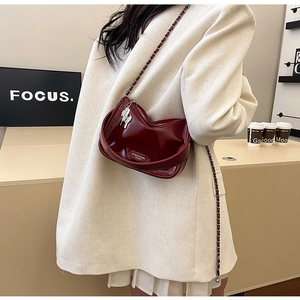 Détail du sac polochon en cuir verni bordeaux foncé avec chaîne argentée et breloque