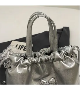 Détail du sac seau argenté avec texture en cuir et décoration de nœud métallique chic