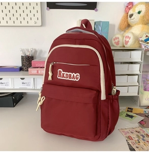 Detail view of burgundy nylon backpack featuring RKDBAG patch and multiple zip pockets