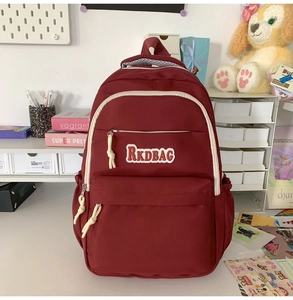 Detailed view of deep red durable nylon backpack with RKDBAG logo on a white desk