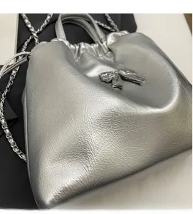 Détail du sac argenté plissé avec nœud métallique et bandoulière en chaîne élégante