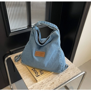 Dettaglio della borsa tote in denim azzurro con toppa in pelle marrone su uno sgabello