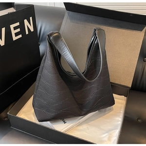 Detailed view of black wavy textured tote bag displayed on books in a luxury box