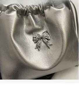 Détail du sac seau argenté avec nœud métallique et texture en cuir synthétique plissé