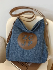 Blue denim hobo shoulder bag with brown leather accents on a white chair setting