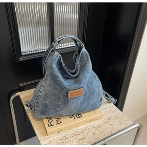 Dettaglio della borsa tote in denim lavato blu con toppa logo in pelle marrone su marmo