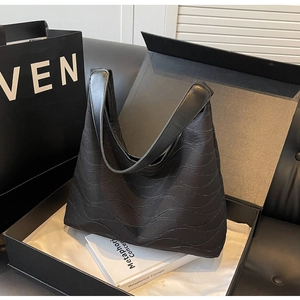 Detail of black wavy quilted hobo tote bag with smooth leather strap in luxury gift box