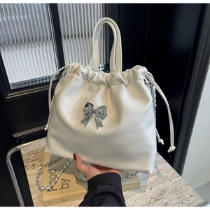 Détail du sac seau blanc à cordon avec nœud argenté et bandoulière en chaîne