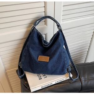 Dettaglio dello zaino in denim blu scuro con logo in pelle marrone su sfondo pulito