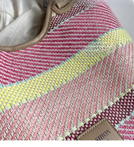 Dettaglio borsa tote in paglia intrecciata rosa e gialla con etichetta in pelle
