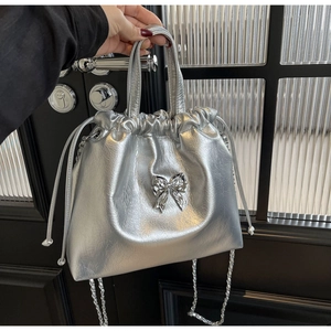 Détail du sac seau argenté avec nœud métallique et bandoulière en chaîne élégante