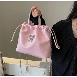 Détail du sac seau en cuir rose avec nœud argenté et bandoulière chaîne tenu par un mannequin