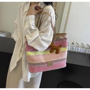 Dettaglio della borsa tote intrecciata a righe colorate con manici in pelle e ciondolo