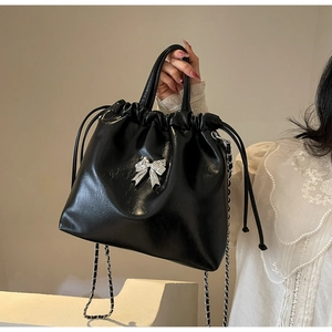 Détail du sac seau noir verni avec un nœud en métal argenté et une bandoulière en chaîne